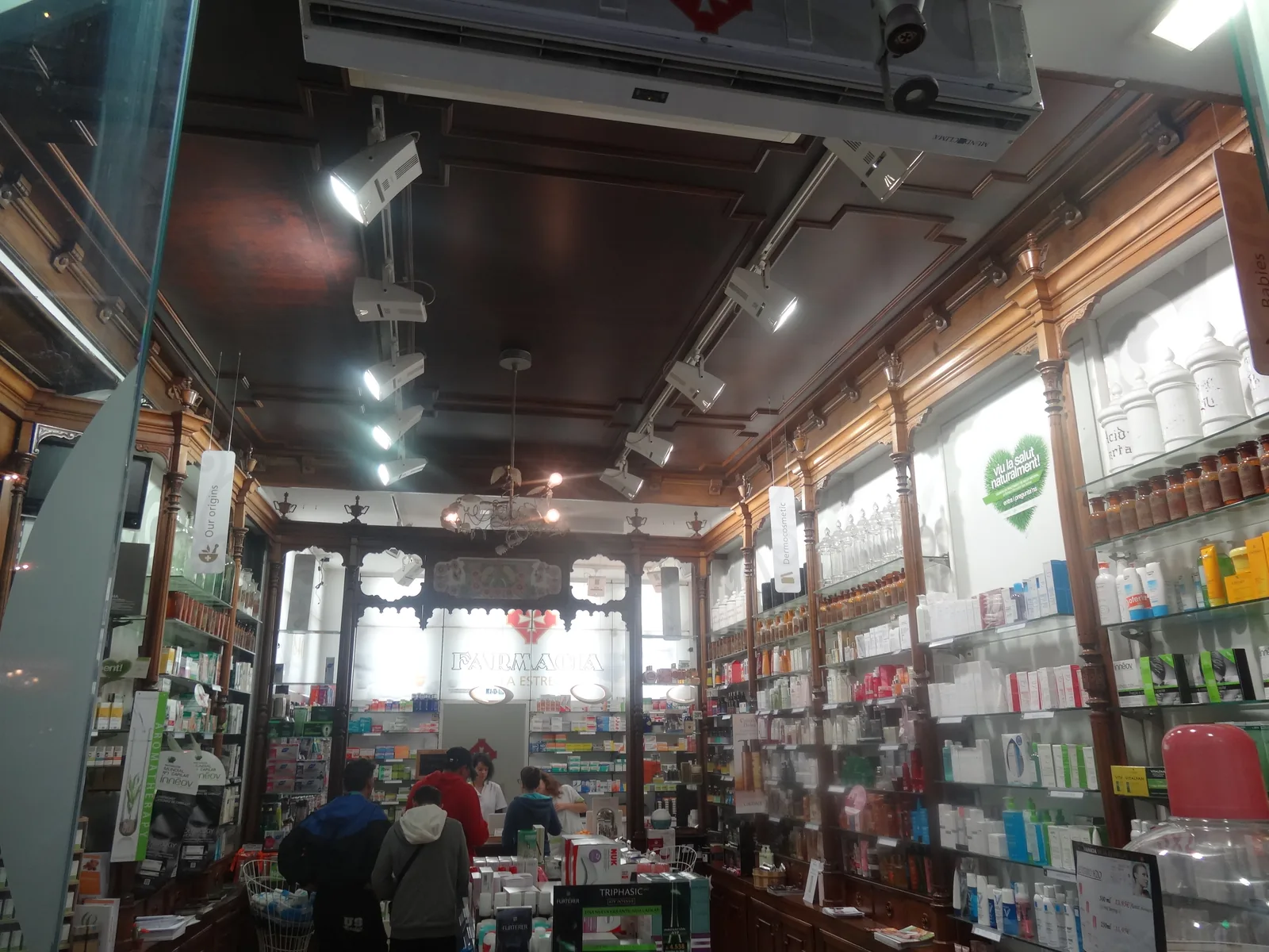 Inside a Barcelona pharmacy with skin care shelves, banners hanging from the ceiling and a cosmetics brand's floor display