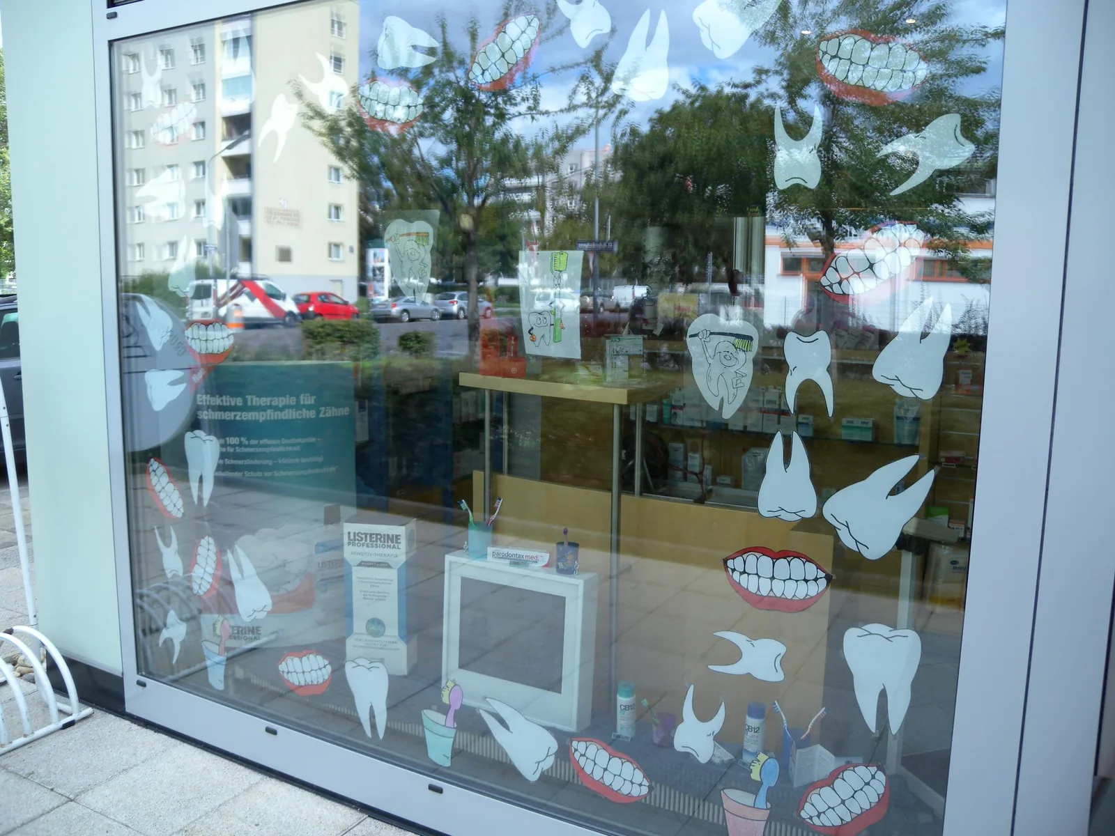 Escaparate de una farmacia con dientes y bocas recortados pegados al cristal, un cartel sobre dientes sensibles y cajas de enjuague bucal y pasta de dientes detrás