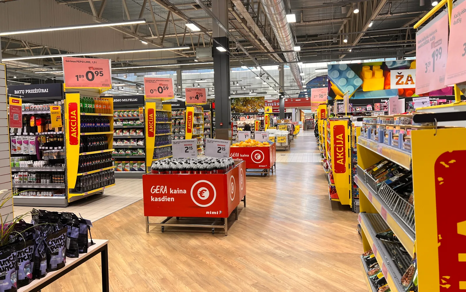 Supermarket aisle with tall yellow and red vertical signs on the ends of the shelving, hanging price signs and two soda islands